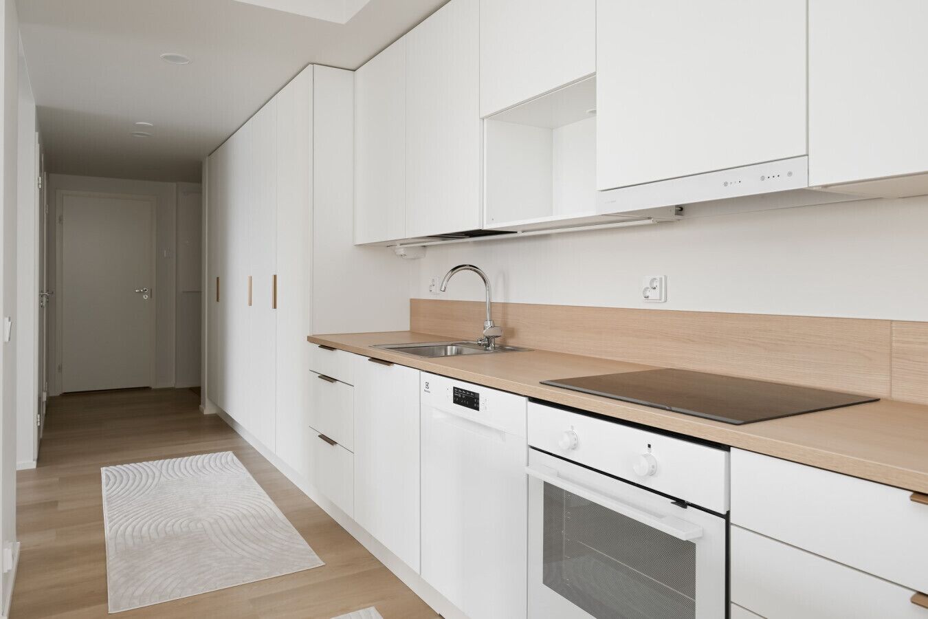 Une cuisine moderne avec des meubles blancs, un évier en acier inoxydable et un four encastré.