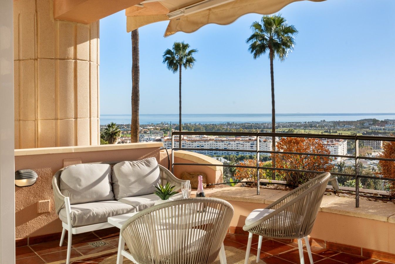 Ein Balkon mit einer Couch und Stühlen, mit Blick auf eine Stadtlandschaft und das Meer.