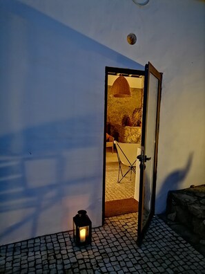 An open door leading to a room with a stone wall, a hanging light fixture, and a lantern on the floor.