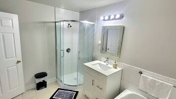 A bathroom with a glass-enclosed shower, a white sink, a mirror with a decorative frame, and a white toilet.