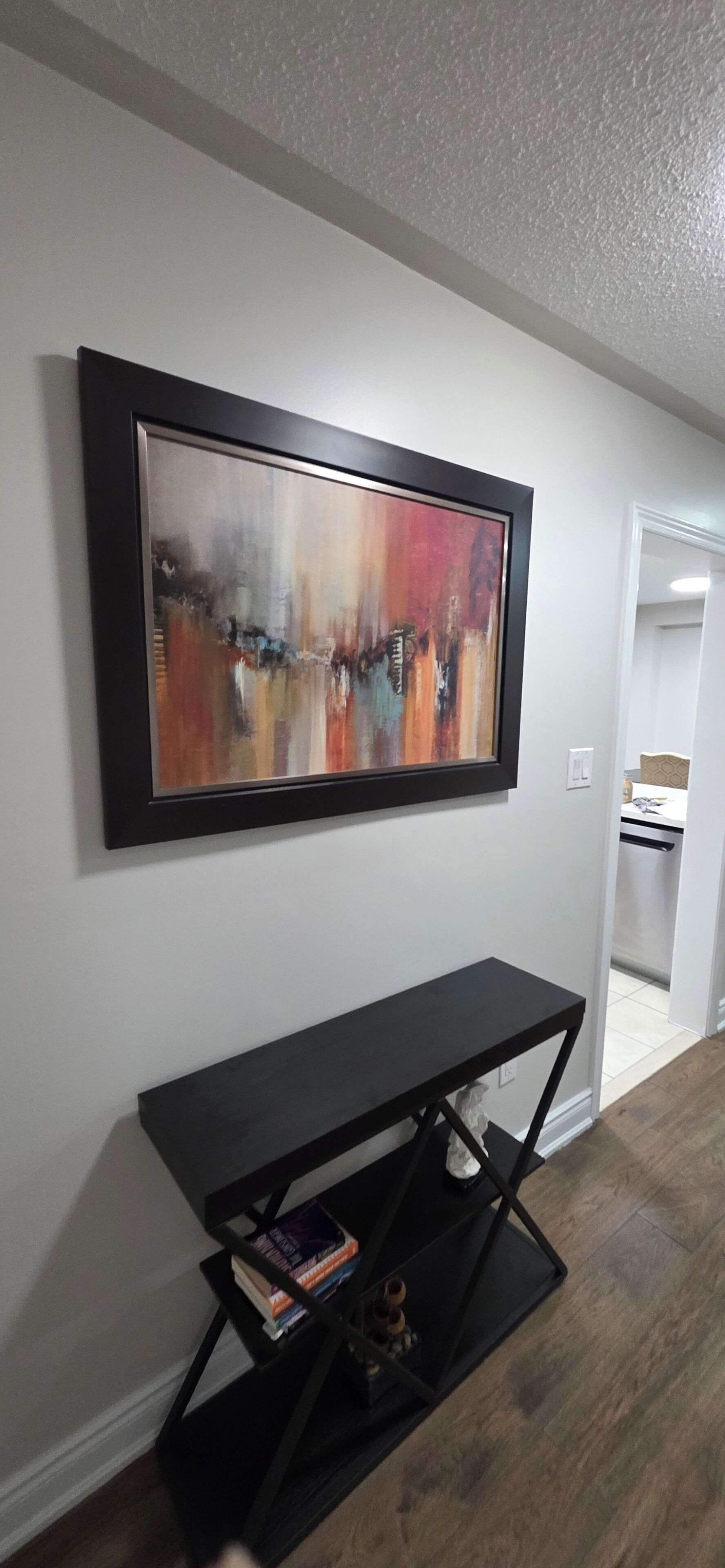 A room with a black console table, a colorful abstract painting, and a doorway leading to a bathroom.