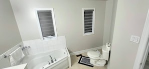 A bathroom with a bathtub, toilet, and two windows. - Cozy Brampton Stay Near Mount Pleasant GO (Brampton)