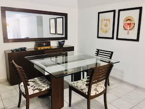 Ein Essbereich mit einem Glastisch, zwei Stühlen mit Blumenmuster-Polsterung, einem dunklen Holzschrank und einem großen Spiegel über dem Tisch.