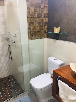 Ein modernes Badezimmer mit Duschkabine aus Glas, einer Wandverkleidung aus Holz, einer weißen Toilette und Ablagefläche aus Glas.