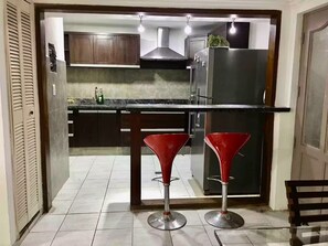 A kitchen with dark wooden cabinets, a stainless steel refrigerator, and two red bar stools.