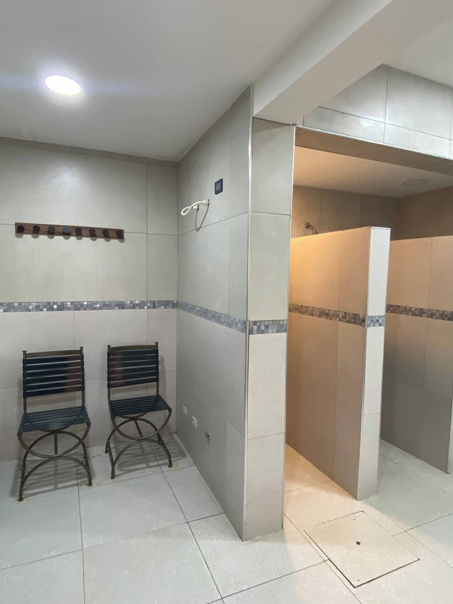 A waiting area with two metal benches, a tiled wall with a decorative border, and a shower stall.
