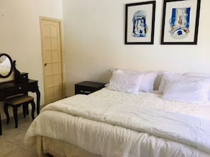 A bedroom with a bed, a dresser, a mirror, and two framed artworks on the wall.