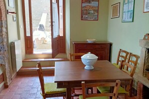 A dining area with a wooden table, chairs, a white bowl, and a stone fireplace. - Grandma Isola's House (Prata)