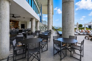 An outdoor seating area with tables and chairs, large concrete columns, and a view of the sea. - Stylish Ocean-View Condo in Downtown Miami (Miami)