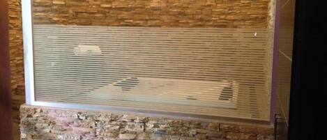 A room with a stone wall, a window with horizontal blinds, and a wooden floor.