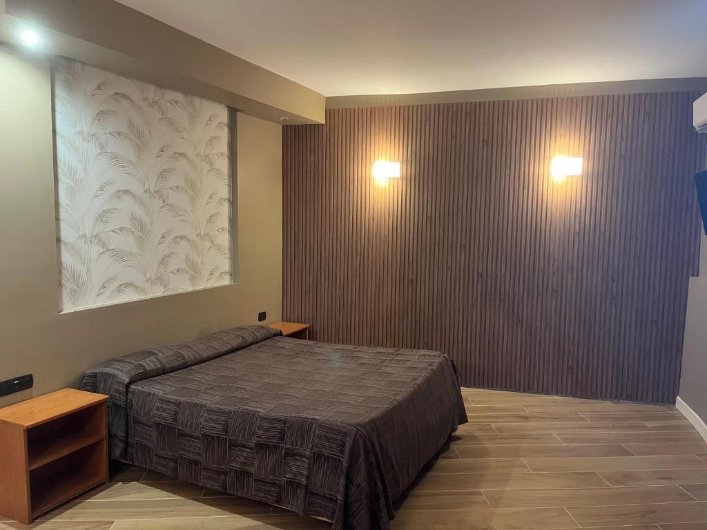 Quarto com cama, mesas de cabeceira, luminária fixada na parede e painel de parede de madeira.