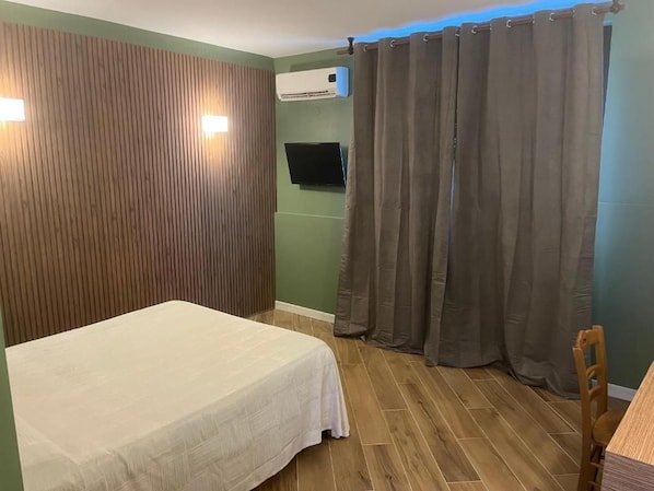 A room with a bed, a flat-screen TV mounted on the wall, and a curtain. - hotel ginepro (Qualiano)