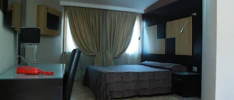Quarto de hotel com cama, escrivaninha, cadeira, mesa de cabeceira e espelho.
