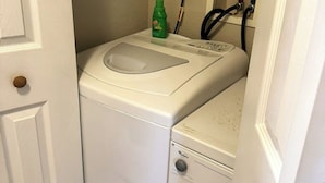 Een compacte wasmachine en droger combinatie met een bedieningspaneel, een groene fles wasmiddel en een stopcontact.
