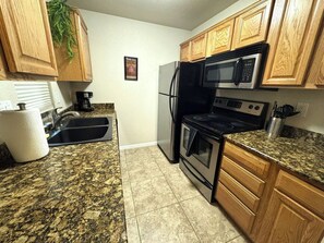 Una cocina con gabinetes de madera, un refrigerador de acero inoxidable, un microondas, una estufa y encimeras de granito.
