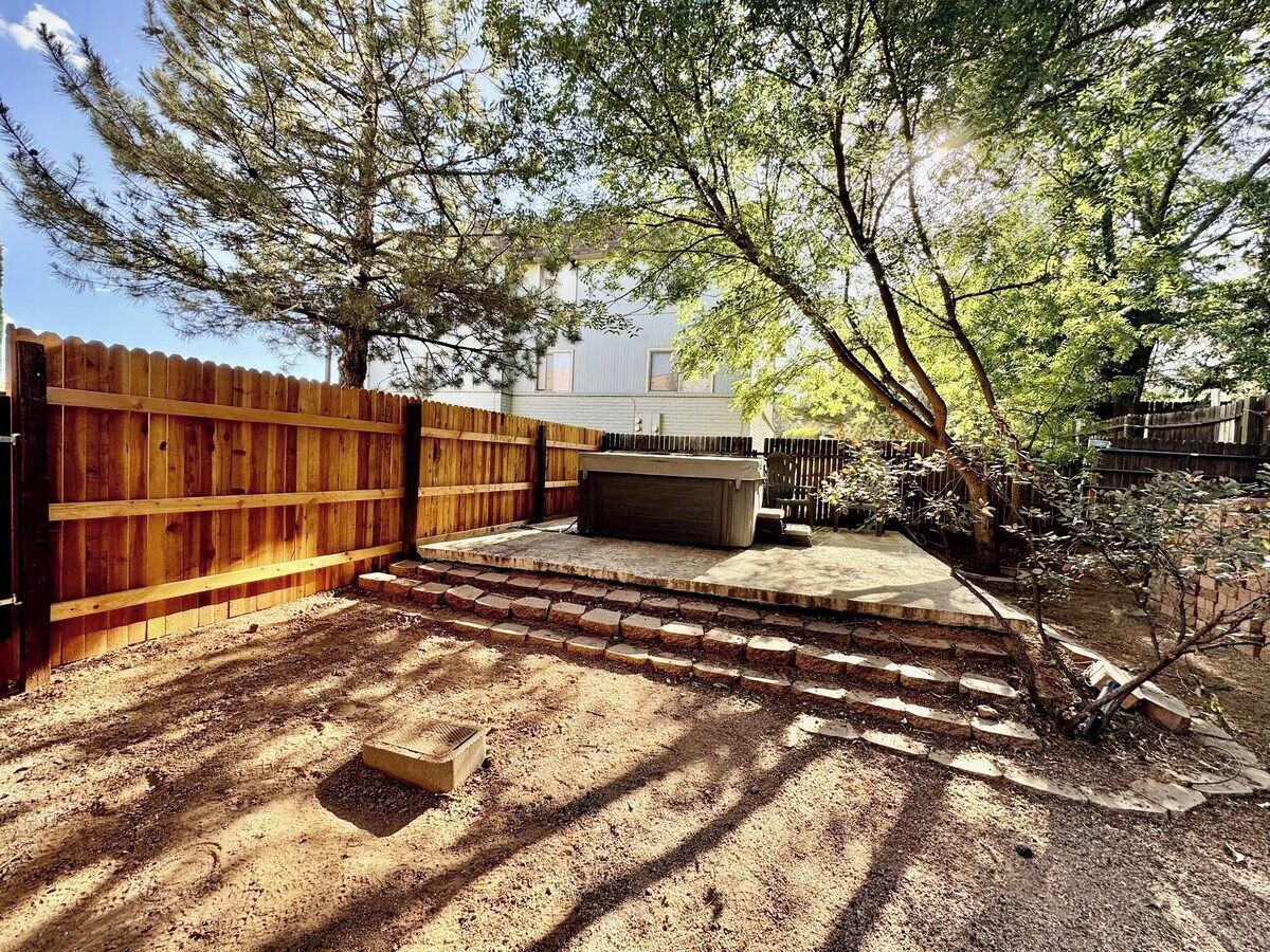 A backyard with a wooden fence, a concrete patio, and a small tree.