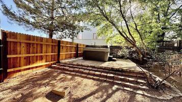 Un patio trasero con cerco de madera, patio de concreto y un árbol pequeño.
