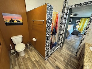 A bathroom with a toilet, a hand dryer, and a shower curtain with a giraffe print. - The Lookout on Andrea | 3BR/2BA Home (Miami)