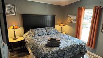 Une chambre à coucher avec un lit, deux tables de chevet avec des lampes, un ventilateur de plafond et une fenêtre avec des rideaux.