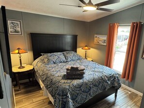 A bedroom with a bed, two bedside tables with lamps, a ceiling fan, and a window with curtains.