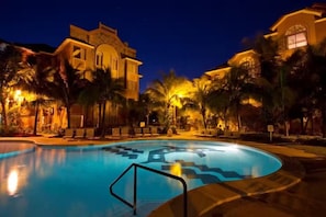 A swimming pool with a geometric design, surrounded by palm trees and a building with arched windows. - Resort 5 Estrellas - Vista a Piscina & Jacuzzi (Santa Cruz de la Sierra)