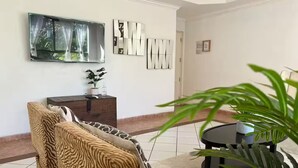 A living room with a sofa, a coffee table, a TV mounted on the wall, and a potted plant.