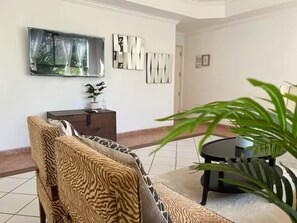 A living room with a sofa, a coffee table, a TV mounted on the wall, and a potted plant.