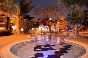 A pool area with a star-shaped design, surrounded by palm trees and buildings with warm lighting. - Resort 5 Estrellas - Vista a Piscina & Jacuzzi (Santa Cruz de la Sierra)