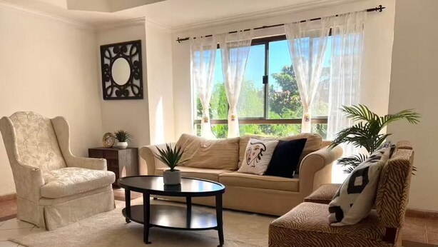 A living room with a sofa, two armchairs, a coffee table, and a decorative mirror.