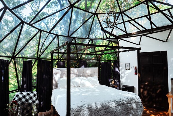 A room with a bed, a chandelier, and a view of the forest through a geometric ceiling structure. - Hotel San Vicente Hideaway (Quesada)