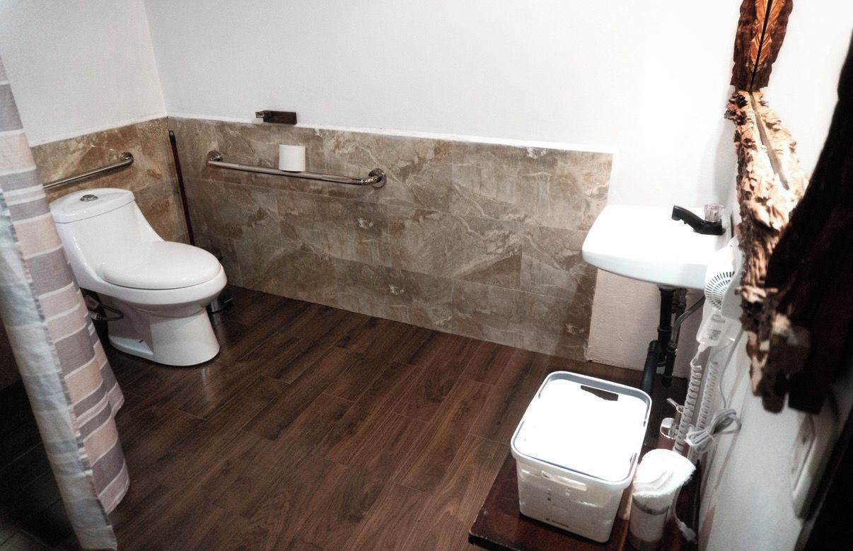 A bathroom with a toilet, a sink, a shower area, and a storage bin.