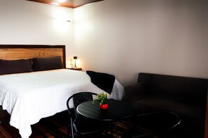 Una habitación de hotel con una cama, una mesita redonda con una silla, un sofá y una mesita de noche con una lámpara.