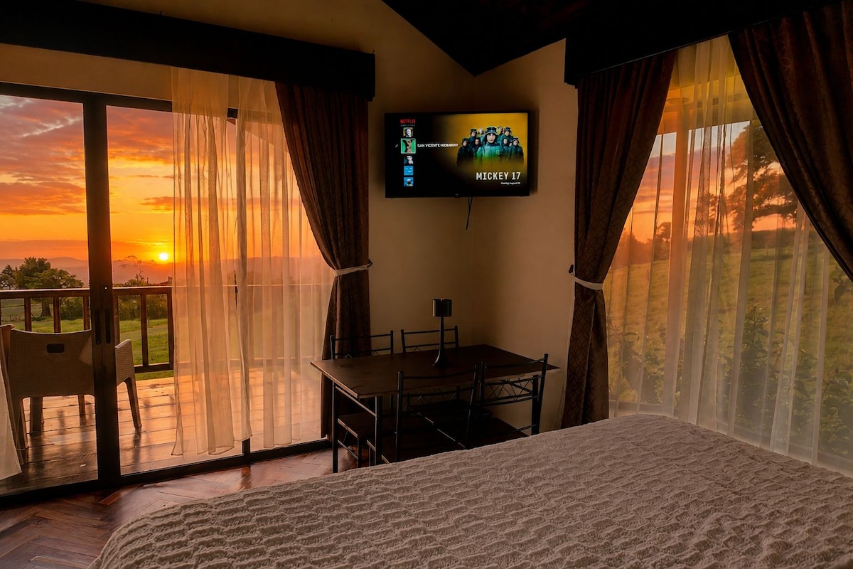 Un dormitorio con cama, televisor montado en la pared, una mesa y sillas.