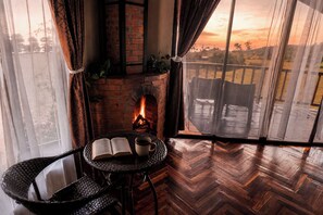A cozy room with a brick fireplace, a table with a book and a cup, and a view of the outdoors.