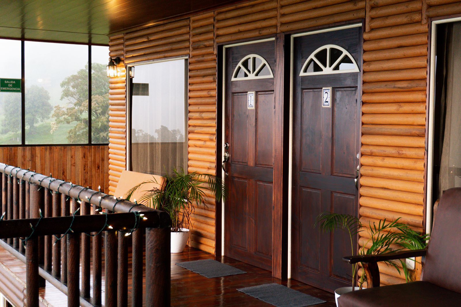 Exterior de madera con dos puertas, un porche cubierto y vistas a árboles.