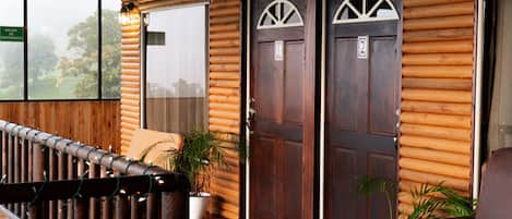 A wooden exterior with two doors, a covered porch, and a view of trees.