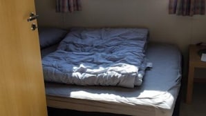 A small bedroom with a single bed, a window with curtains, and a door.