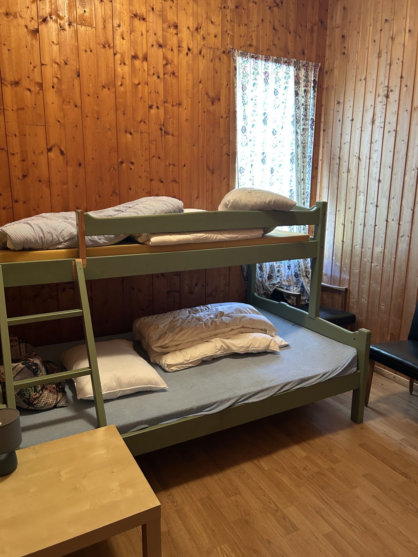 Habitación con literas, paredes de madera, una ventana con cortinas florales y una mesita.