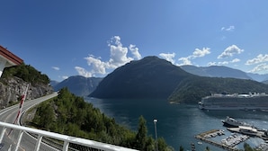A coastal landscape with a road, mountains, and a cruise ship docked at a marina.
