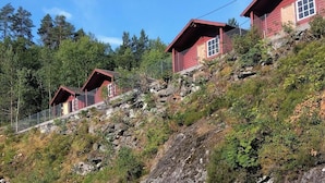 Una cabaña roja con un porche de madera, rodeada por una ladera boscosa.