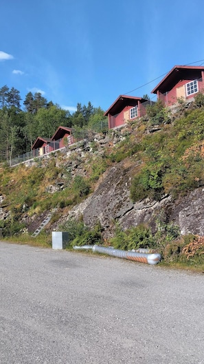 Eine rote Holzhütte mit einer Holzterrasse, umgeben von einem bewaldeten Hang.