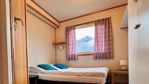 Una habitación pequeña con cama individual, ventana, mesita de noche y lámpara.