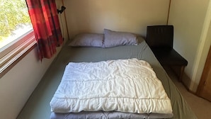 Una habitación pequeña con cama, una mesita y ventana con cortinas.
