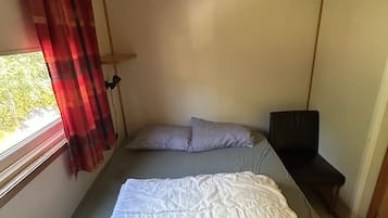 Una habitación pequeña con cama, una mesita y ventana con cortinas.