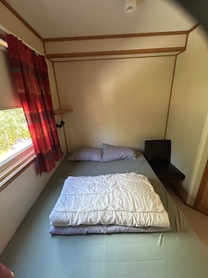 Ein kleines Zimmer mit einem Bett, einem kleinen Tisch und einem Fenster mit Vorhängen.
