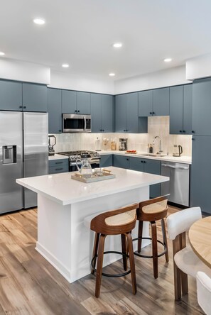 A modern kitchen with a central island, bar stools, and a dining table.