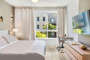 Et moderne hotelværelse med en stor seng, et skrivebord, en stol, et fjernsyn og udsigt udad.