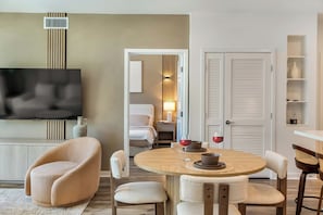 A modern living room with a flat-screen TV, a round dining table, and a cozy seating area.