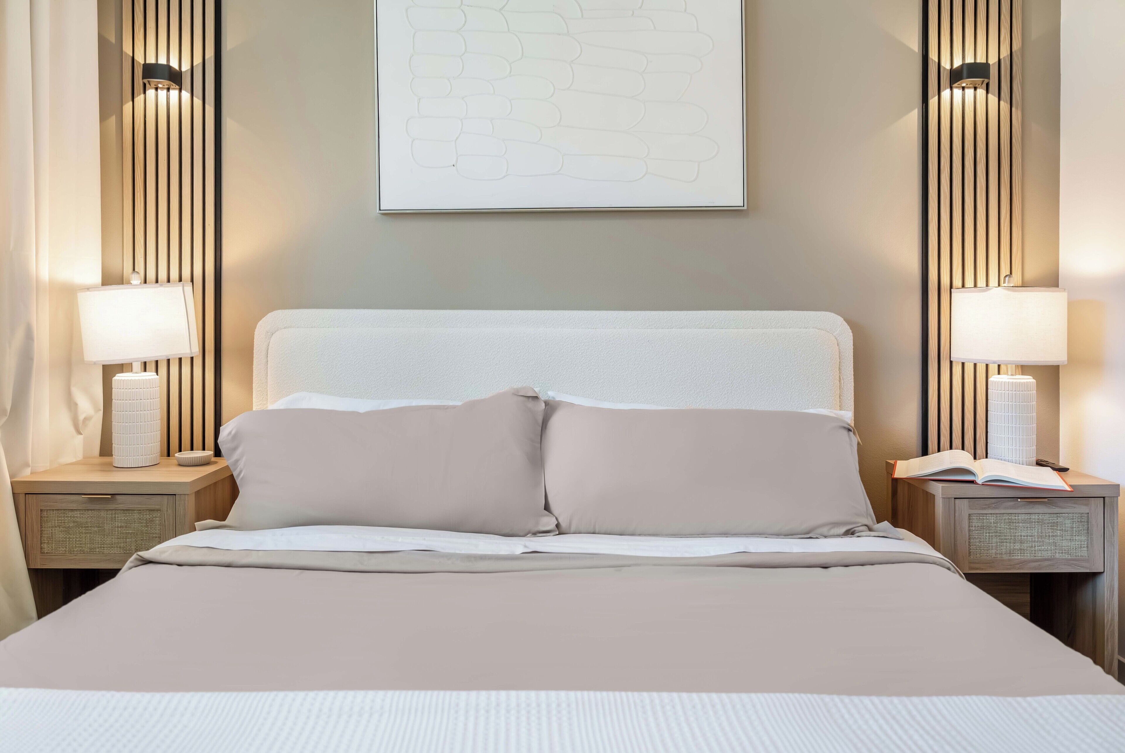 Un letto rifatto con cura, una testiera, due lampade ai comodini e un'opera d'arte appesa al muro.