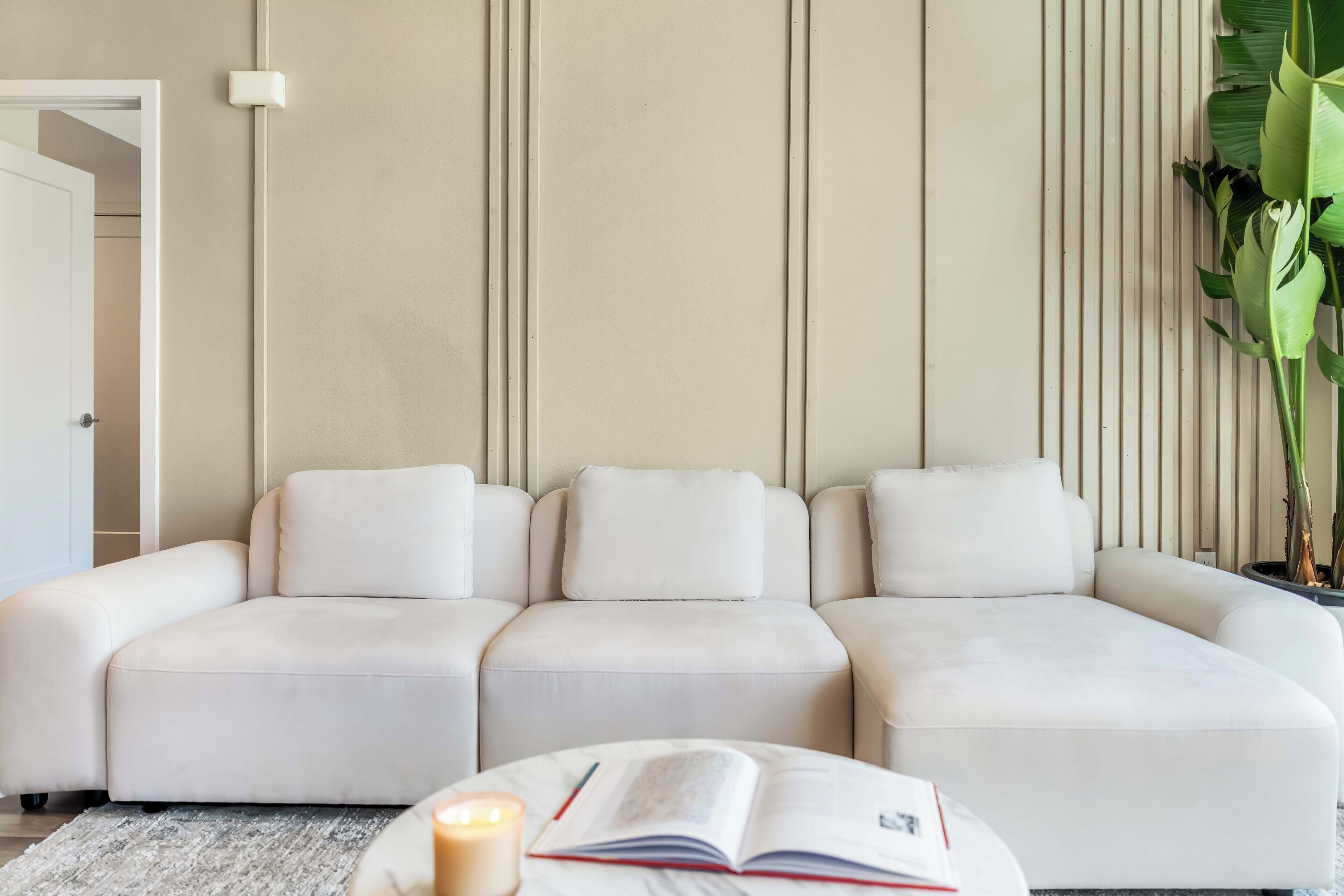 A modern living room with a sectional sofa, a book, and a candle on a table.